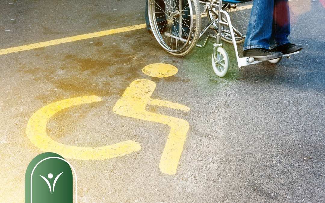 Symbol osoby z niepełnosprawnością namalowany na nawierzchni parkingu. Widoczny fragment wózka inwalidzkiego i nogi osoby siedzącej na wózku.