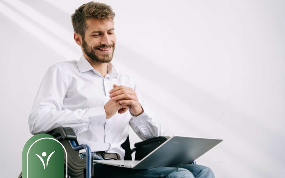 Uśmiechnięty mężczyzna siedzący na wózku inwalidzkim, korzystający z laptopa. Grafika symbolizuje samodzielność i dostęp do usług elektronicznych, w tym składanie wniosku o świadczenie wspierające online.