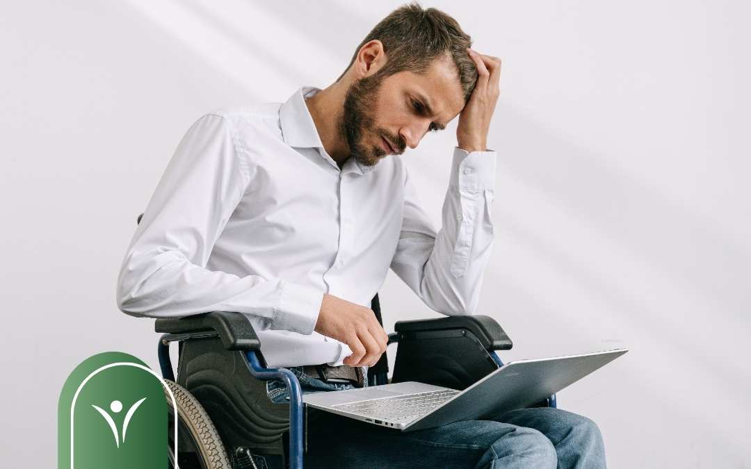 Mężczyzna poruszający się na wózku inwalidzkim, siedzący przy laptopie. Grafika ilustrująca trudności związane z decyzją WZON i świadczeniem wspierającym.