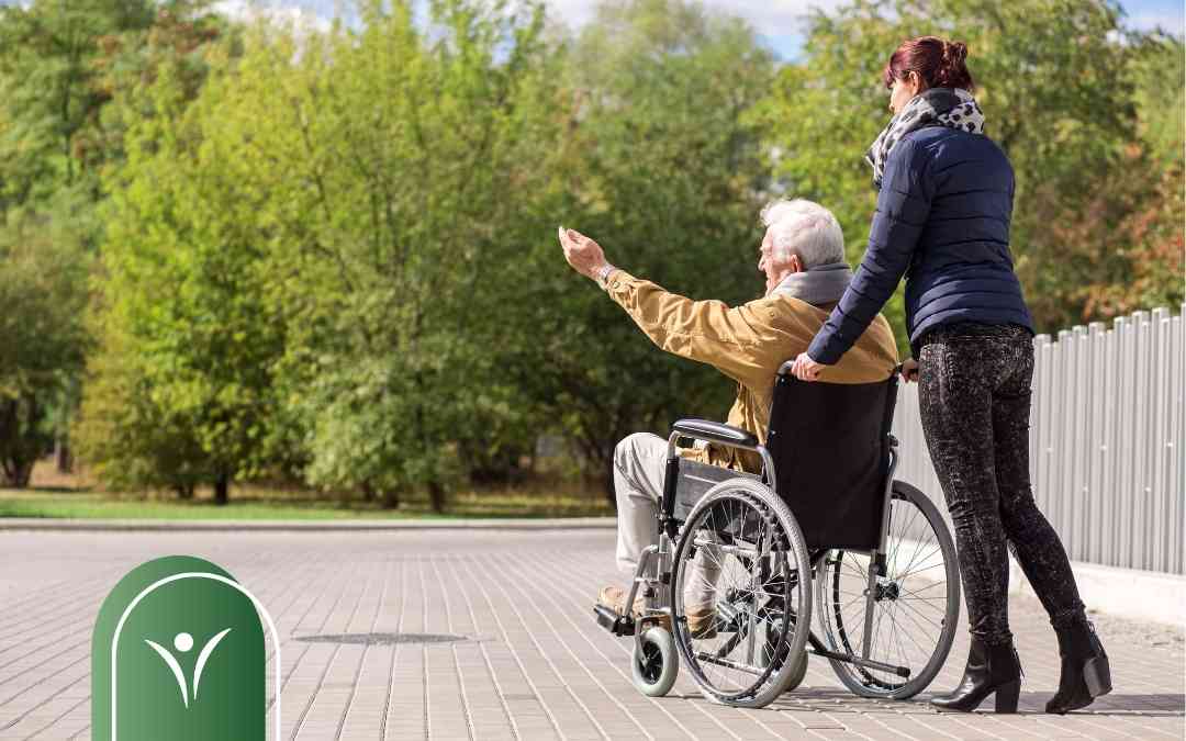 Asystentka prowadzi mężczyznę na wózku inwalidzkim. Przykład codziennego wsparcia w mobilności i pokonywaniu barier.