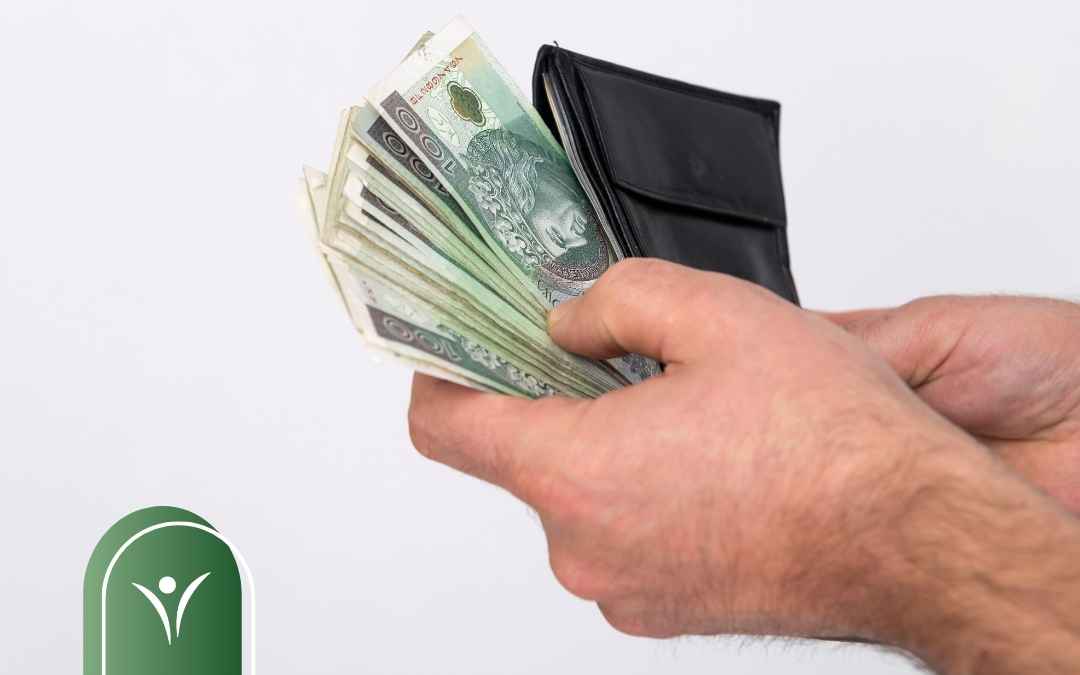 Męskie dłonie wyjmujące plik banknotów o nominale 100 złotych z czarnego portfela.