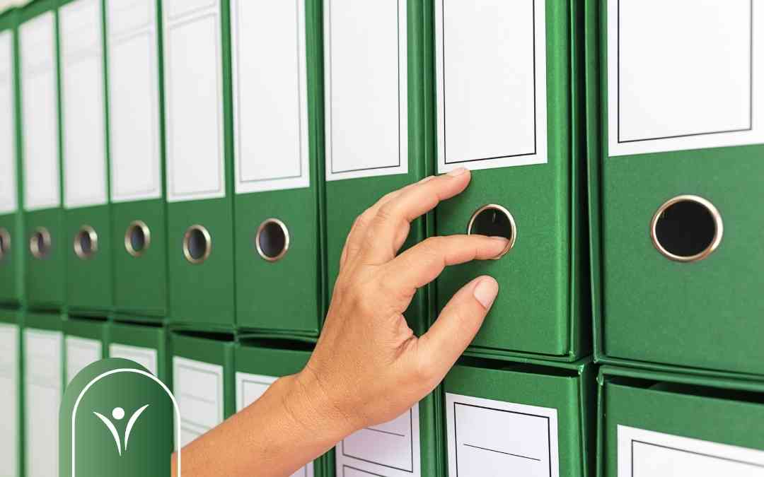 Dłoń wybierająca zielony segregator z dokumentacją – przygotowanie wniosku o ustalenie poziomu potrzeby wsparcia.