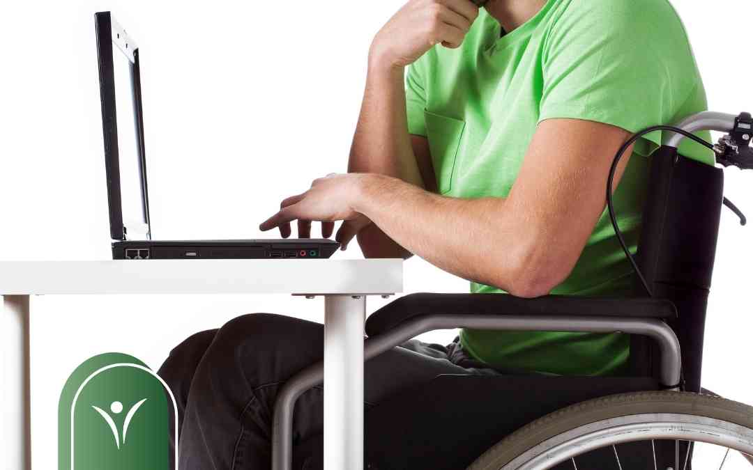 Mężczyzna w zielonej koszulce siedzący na wózku inwalidzkim wypełnia elektroniczny wniosek o świadczenie wspierające na laptopie.