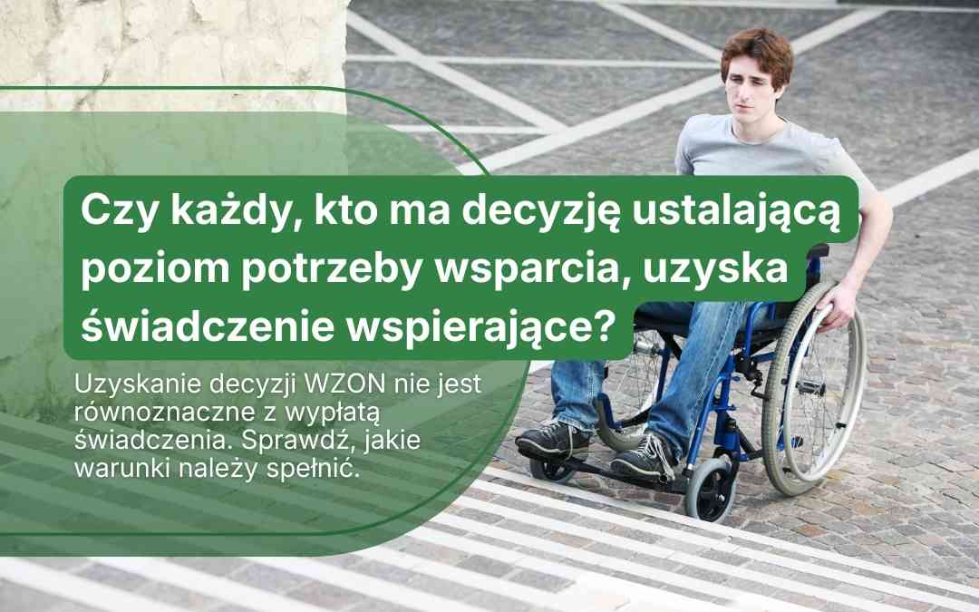 Mężczyzna na wózku inwalidzkim na zewnątrz obok planszy informacyjnej o warunkach uzyskania świadczenia wspierającego.