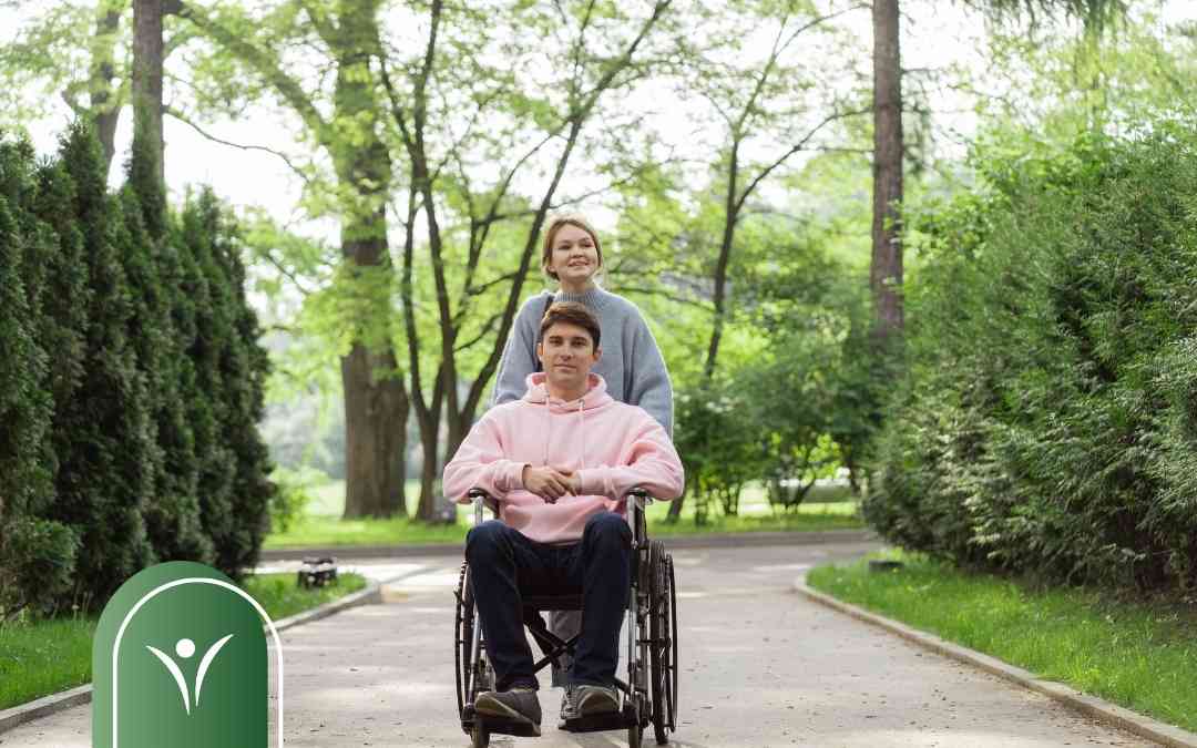 Młody mężczyzna na wózku i kobieta spacerujący w parku.