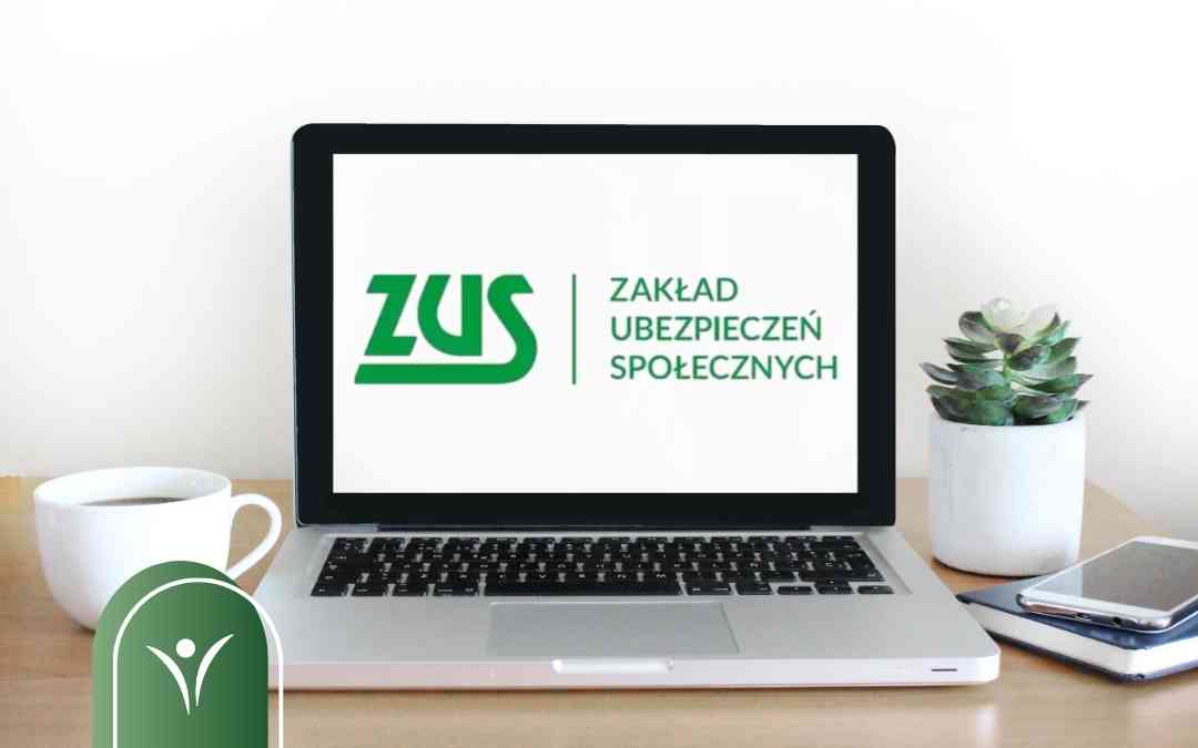 Laptop z wyświetlonym logo ZUS i napisem Zakład Ubezpieczeń Społecznych stojący na biurku. Po prawej roślina, telefon komórkowy i notatnik. Po lewej biała filiżanka.
