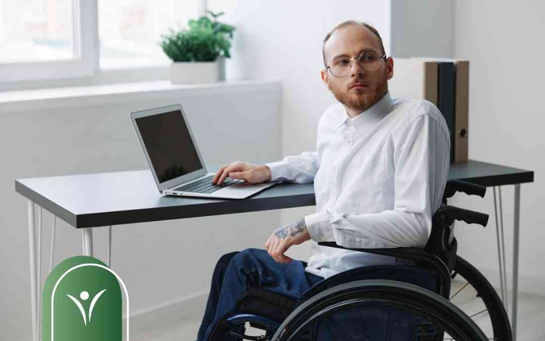 Mężczyzna na wózku inwalidzkim pracuje przy biurku na laptopie – ilustracja do łączenia pracy ze świadczeniem wspierającym.