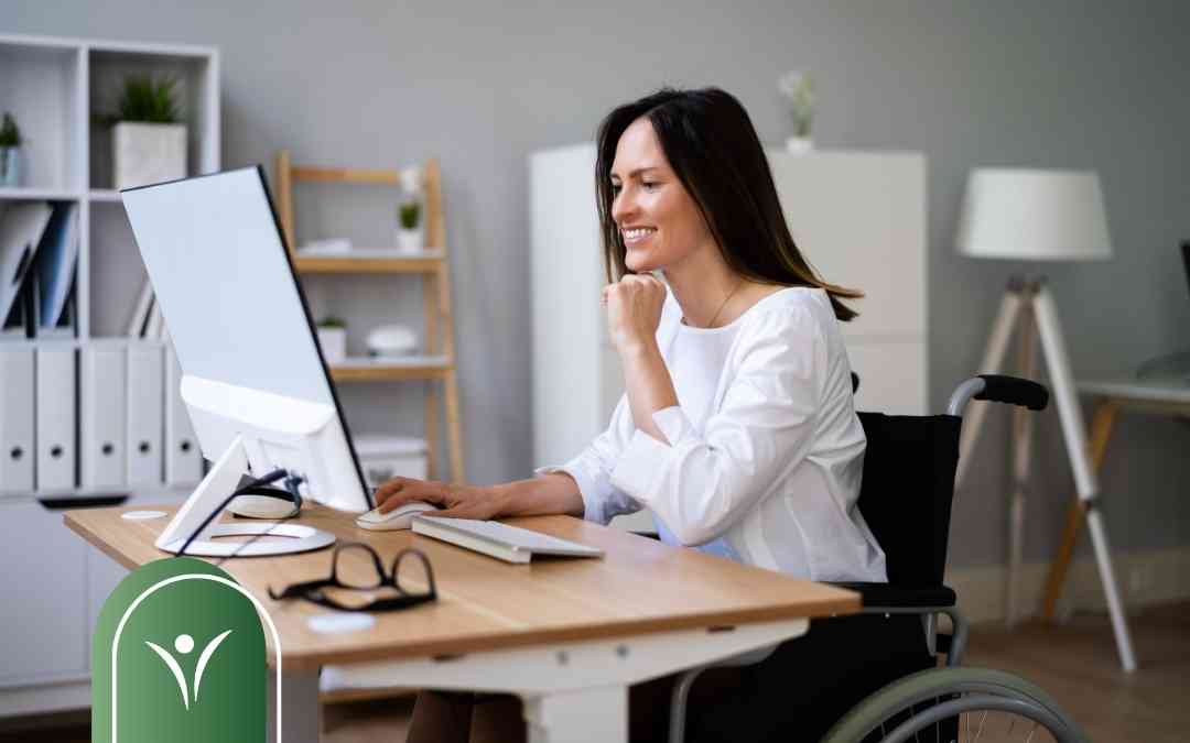 Uśmiechnięta kobieta na wózku inwalidzkim pracuje przy komputerze – ilustracja do artykułu o składaniu wniosku o świadczenie wspierające.