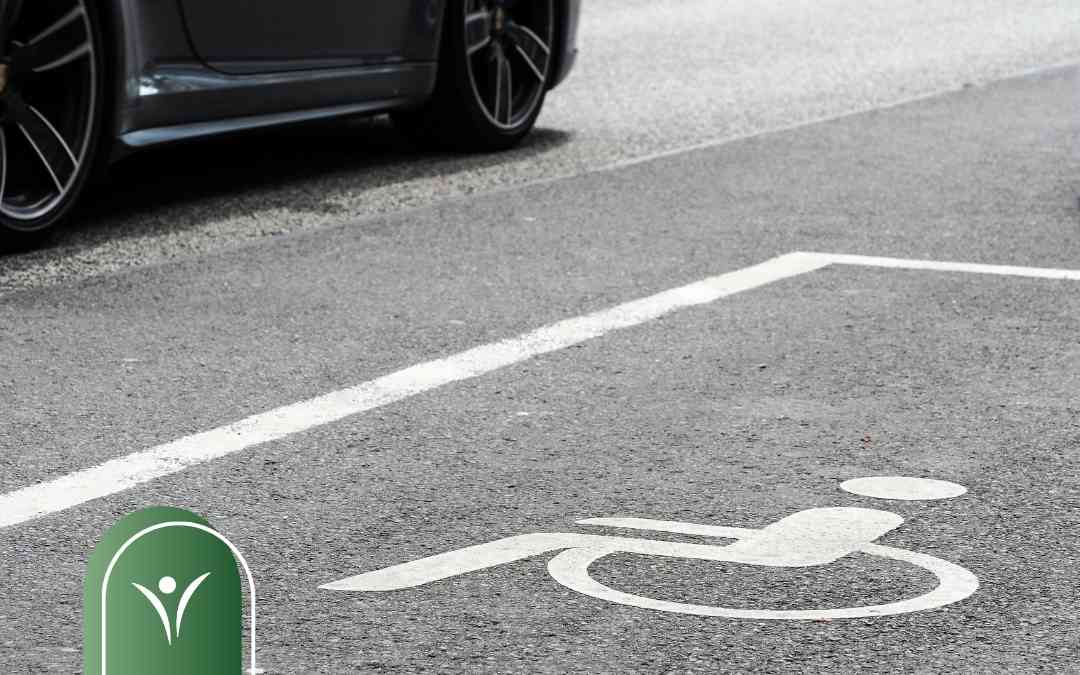 Biały symbol osoby na wózku namalowany na asfalcie wyznacza miejsce parkingowe dla niepełnosprawnych.