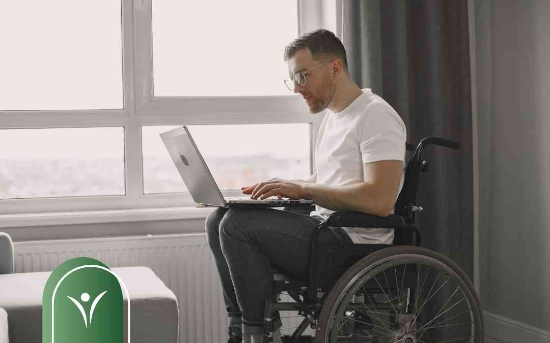 Mężczyzna na wózku inwalidzkim składa elektroniczny wniosek o świadczenie wspierające na laptopie.