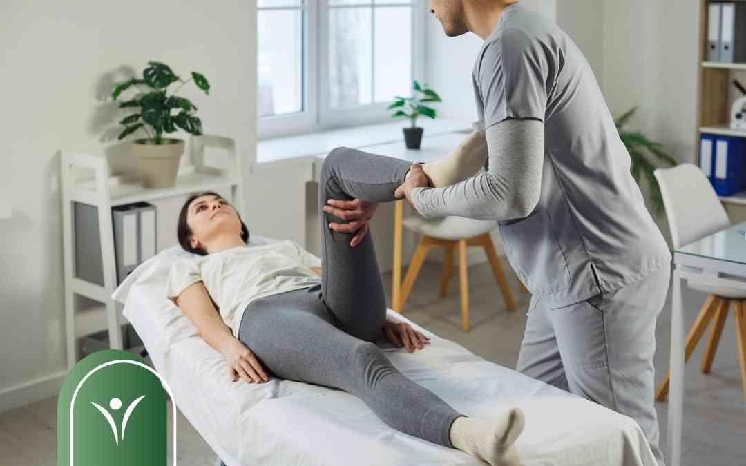 Fizjoterapeuta wykonuje ćwiczenia rehabilitacyjne nogi pacjentki leżącej na stole medycznym.
